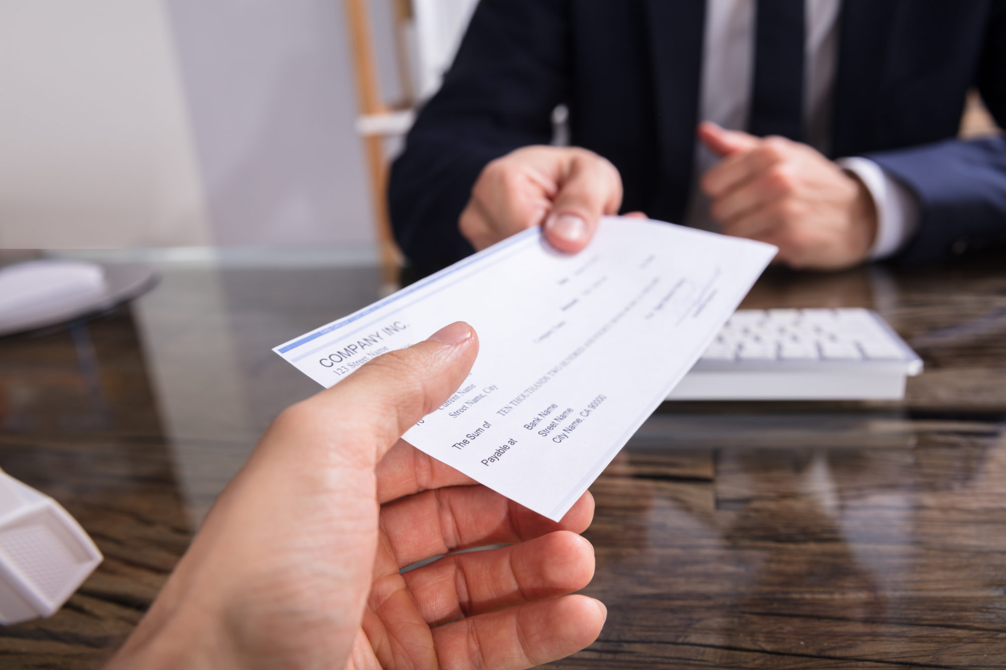 Close Up,Of,A,Businessperson's,Hand,Giving,Cheque,To,Colleague,At